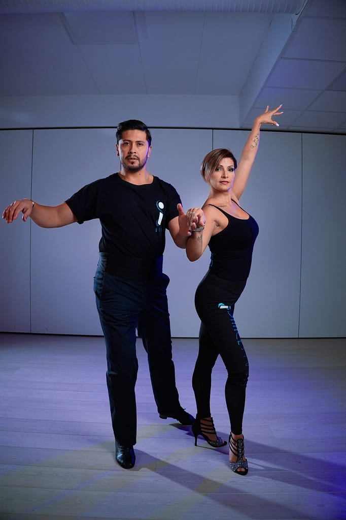 Two dancers in black iDance clothing in a partner dance pose.